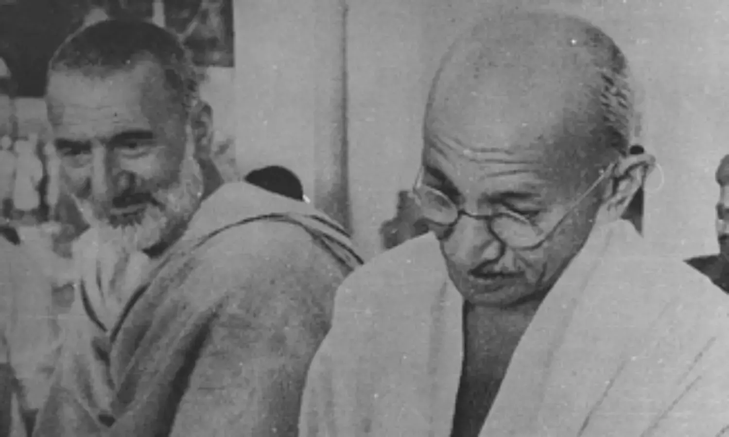 Grainy black and white photograph: Ghaffar Khan on the left in a shawl, listening; Mahatma Gandhi on the right, head lowered, in a white shawl and round spectacles.